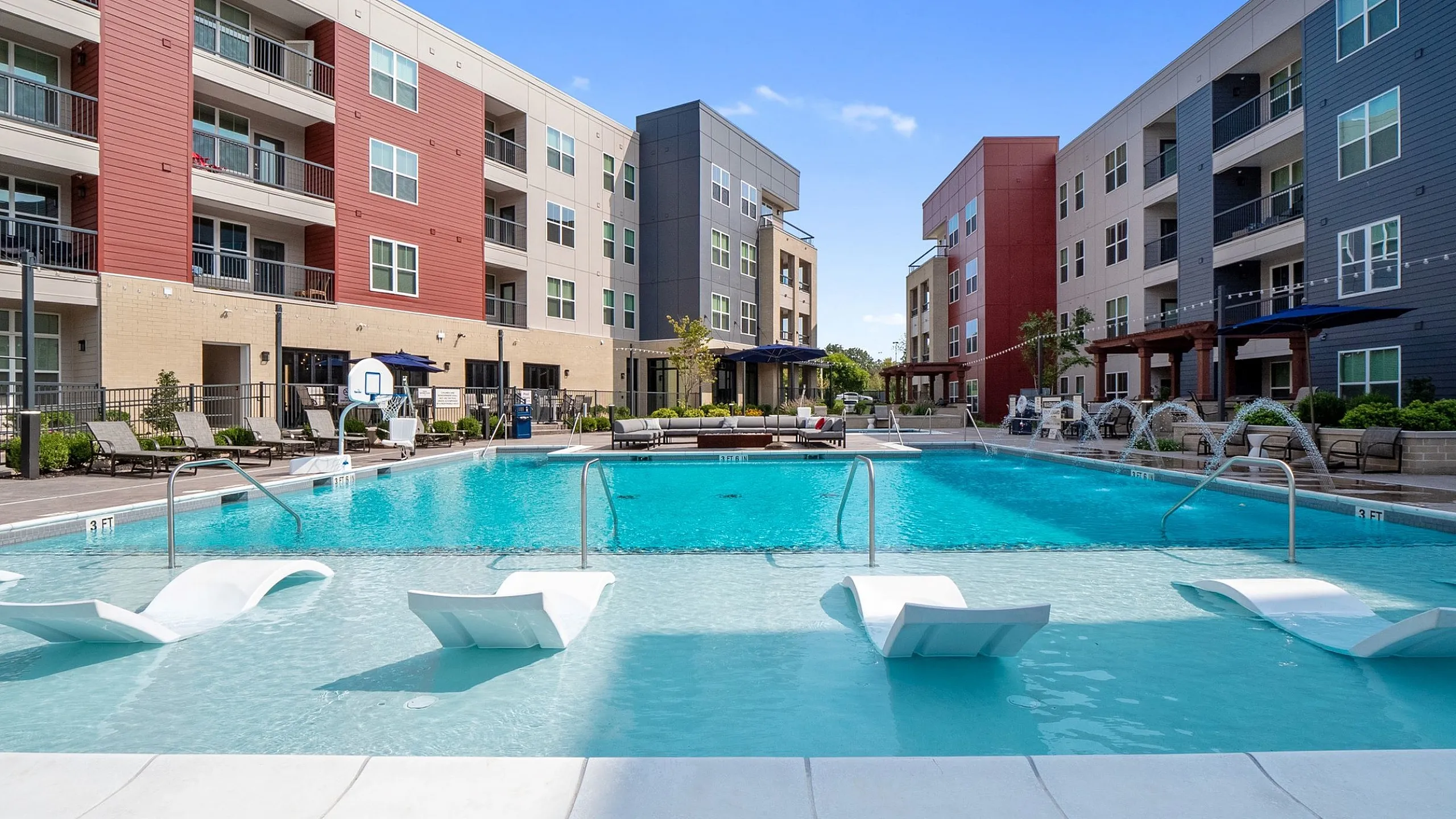 Vibrant apartment complex with a modern pool area featuring loungers and a clear blue sky.