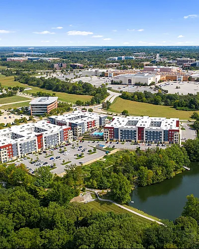 Aerial view of modern apartment complex surrounded by lush greenery and overlooking a serene lake.