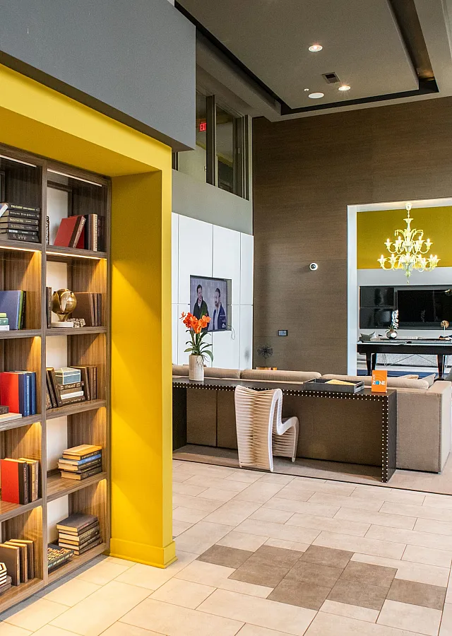 Elegant apartment community lounge featuring a stylish bookshelf, modern seating area, and hanging chandelier.