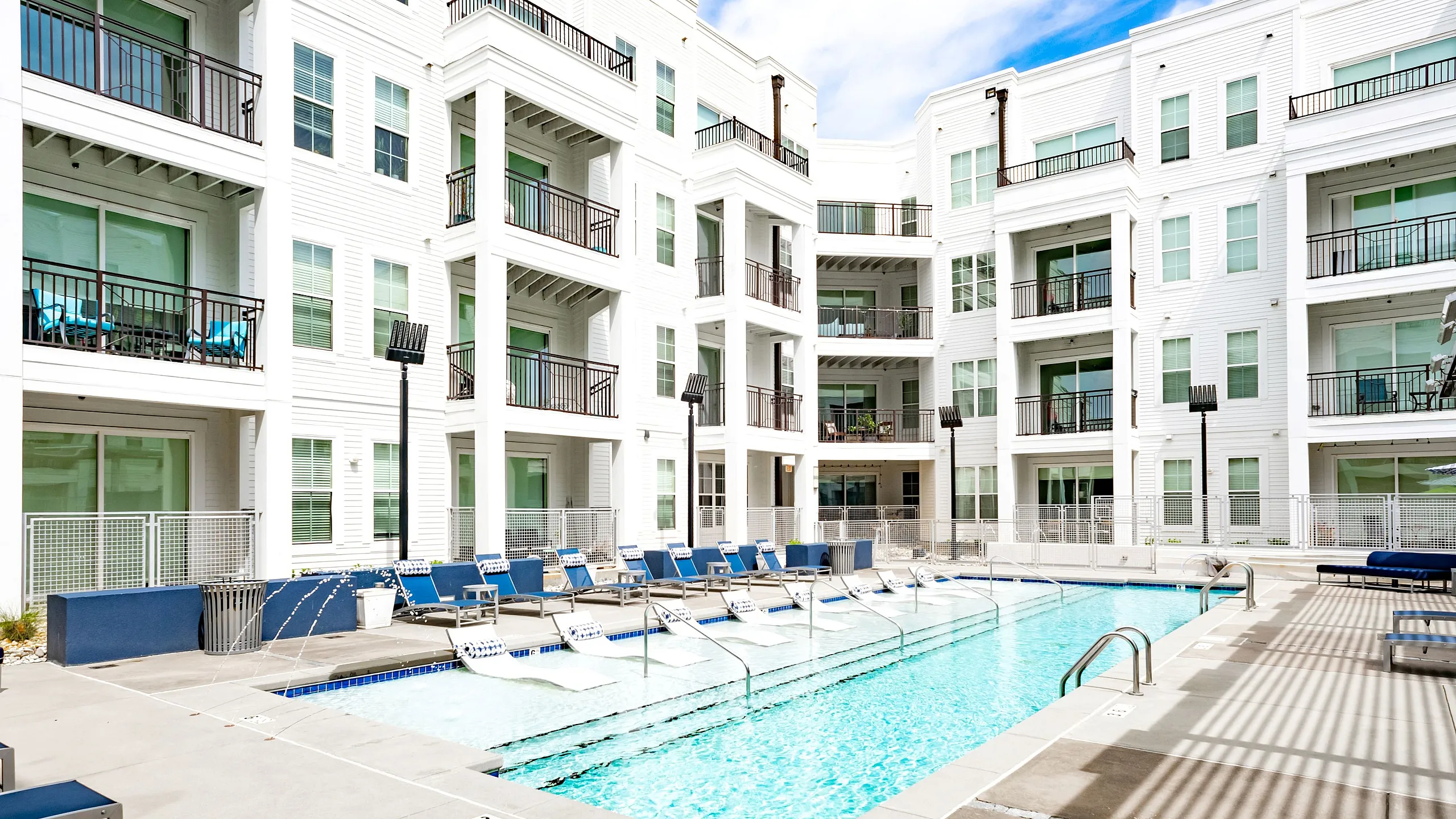 Beautiful apartment complex featuring a modern outdoor pool with lounging chairs and balconies overlooking the area.