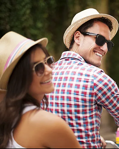 Smiling couple wearing hats and sunglasses riding a bicycle together in a charming street.