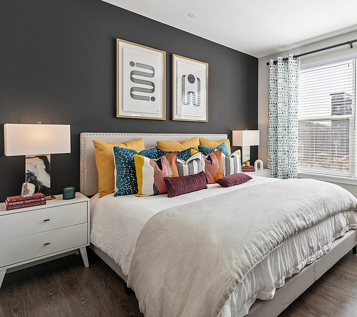 Chic and inviting bedroom featuring a plush king-size bed with vibrant pillows, elegant lamps, and a stunning city view through large windows.