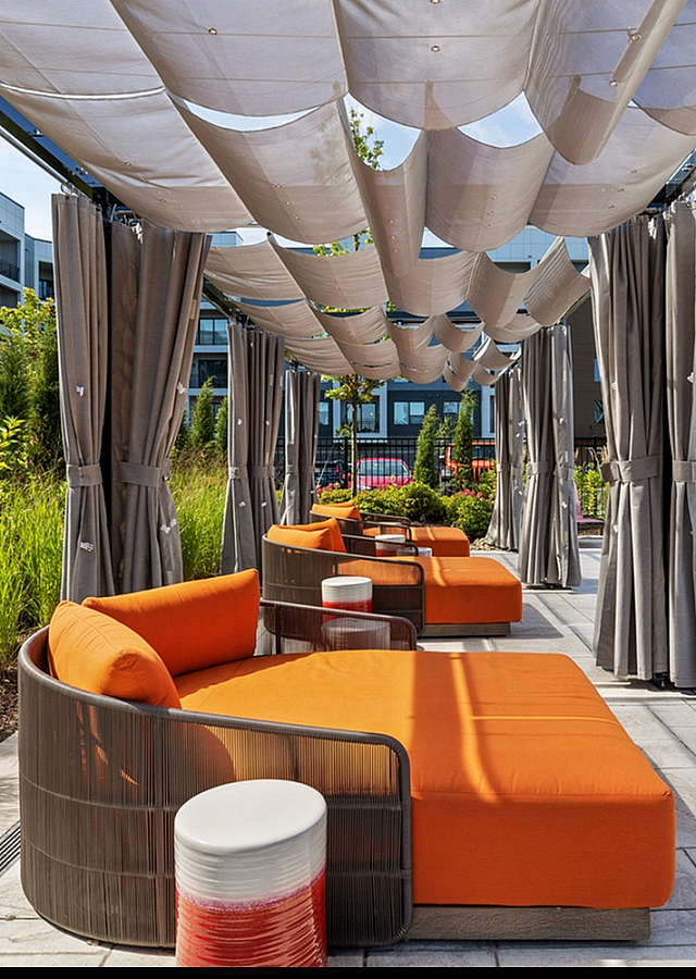 Luxurious poolside cabanas with vibrant orange loungers, set against modern apartment buildings and lush greenery, offering a perfect outdoor retreat.