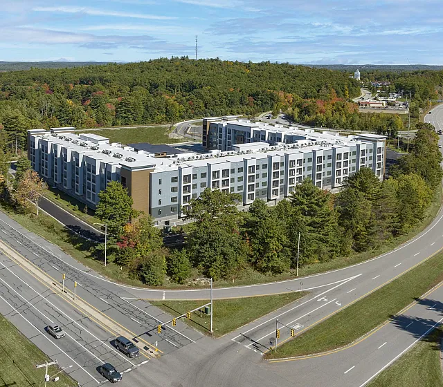 Modern apartment complex surrounded by lush greenery, featuring sleek architecture and convenient road access.