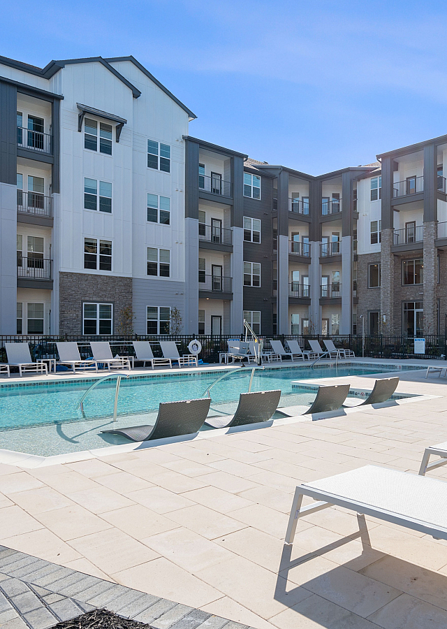 Modern apartment complex with a pristine outdoor pool and stylish lounge chairs, perfect for relaxation and recreation.