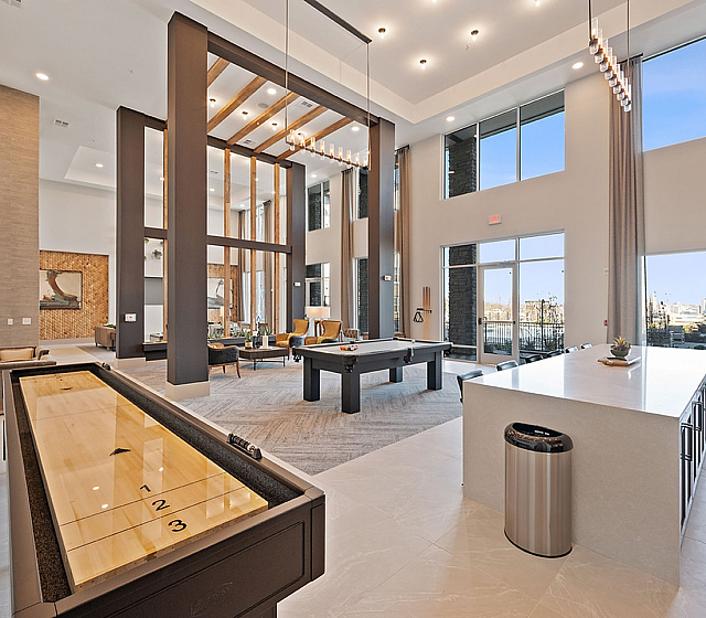 Luxurious open-concept communal space with soaring ceilings, a sleek shuffleboard and pool table, surrounded by floor-to-ceiling windows offering panoramic city views.