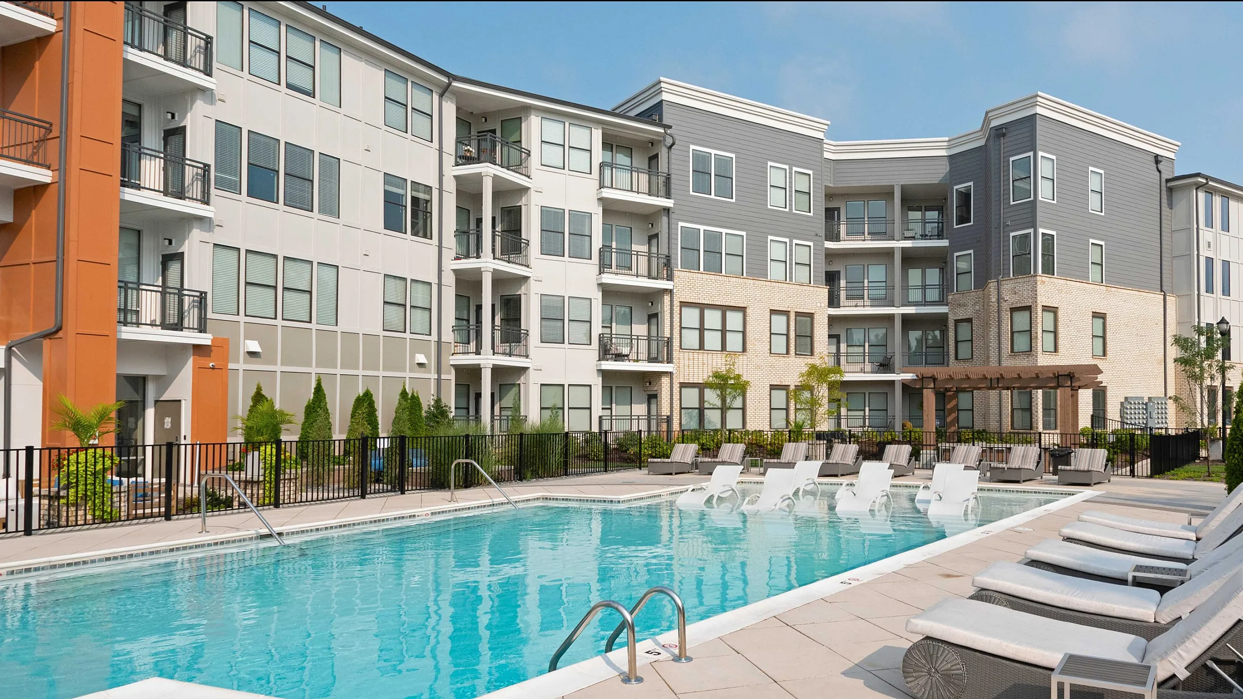Modern apartment complex with luxurious poolside lounging area, surrounded by beautiful landscaping and contemporary architecture.