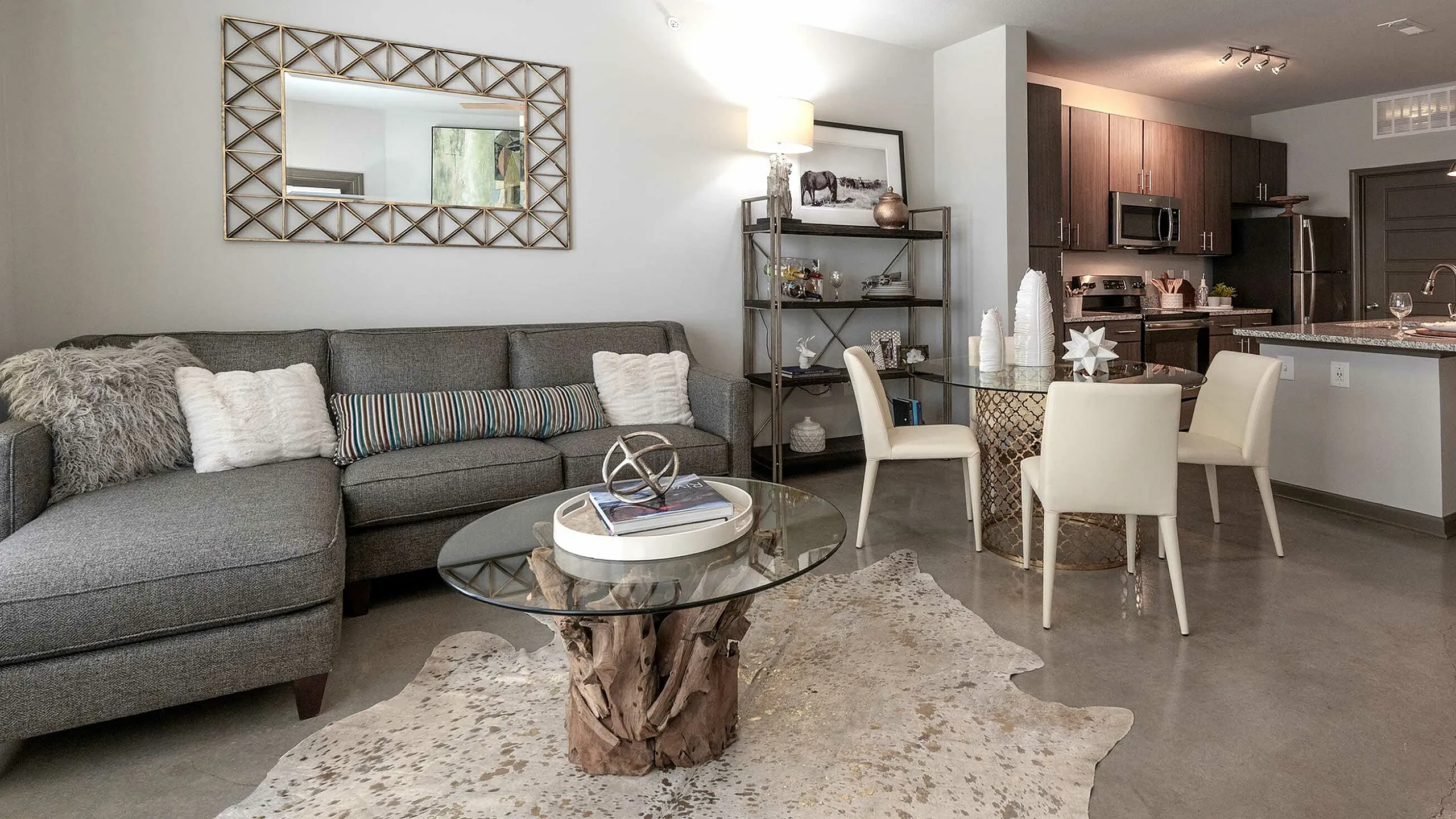 Chic modern apartment living room with a plush grey sectional, stylish glass coffee table on a textured rug, and open-plan kitchen for seamless entertaining.