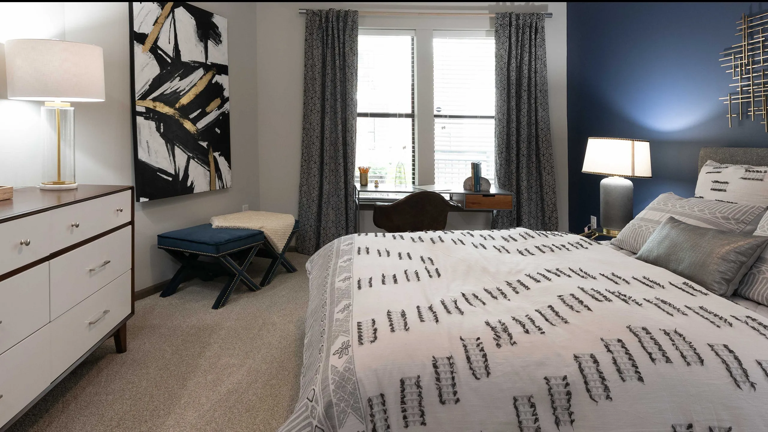 Elegant bedroom with modern decor, featuring a plush bed with patterned bedding, stylish artwork, and a sleek dresser under a decorative mirror.
