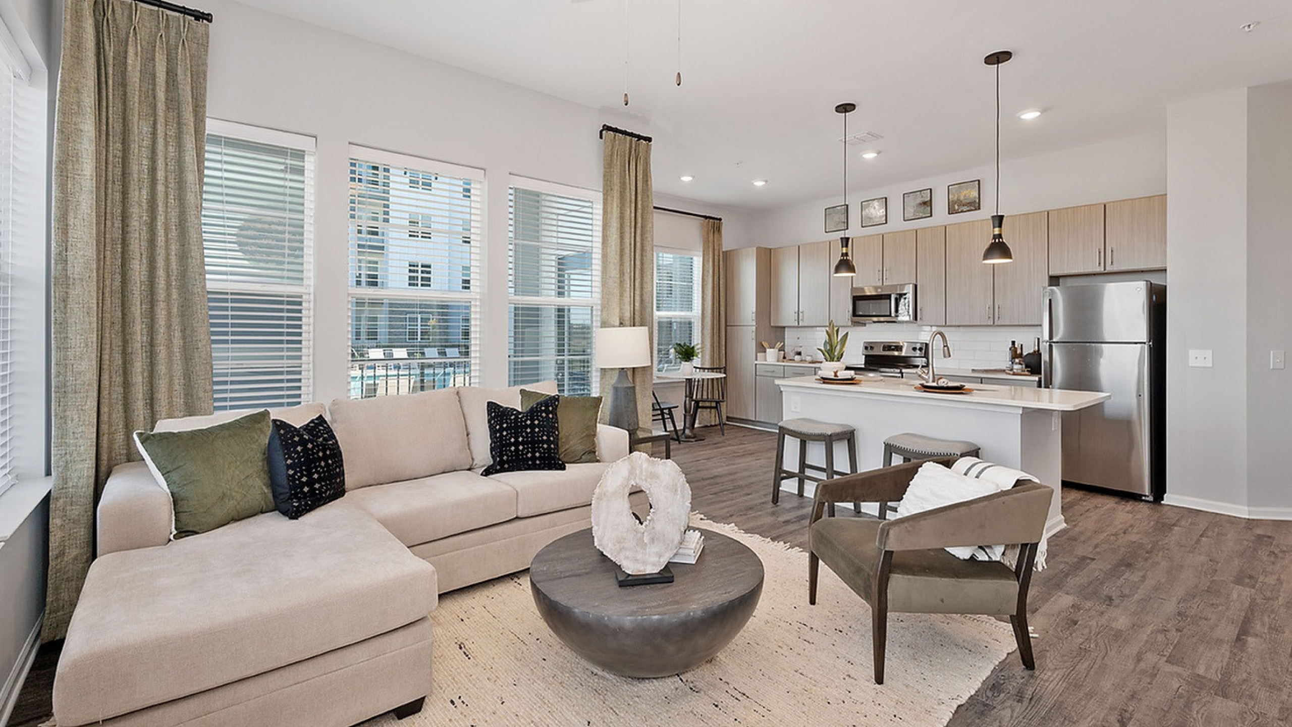 Inviting open-plan living room and kitchen with modern decor, featuring a cozy beige sectional sofa, wood flooring, and stylish pendant lighting.