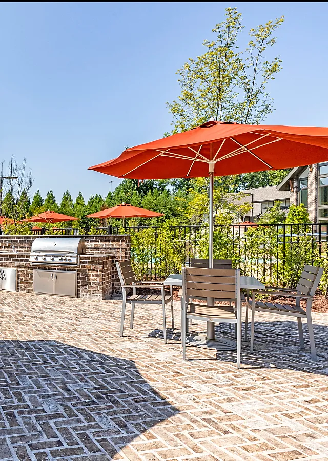 Inviting outdoor patio with modern grills, vibrant orange umbrellas, and stylish seating, perfect for summer gatherings.