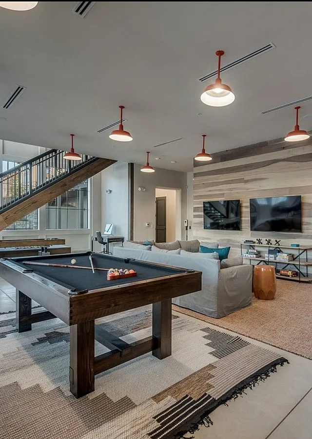 Chic entertainment room featuring a modern pool table, cozy seating area, and sleek flat-screen TVs, bathed in natural light from large windows.