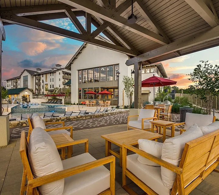 Elegant apartment complex with a beautiful poolside lounge and stunning sunset views, featuring comfortable outdoor seating and vibrant umbrellas.