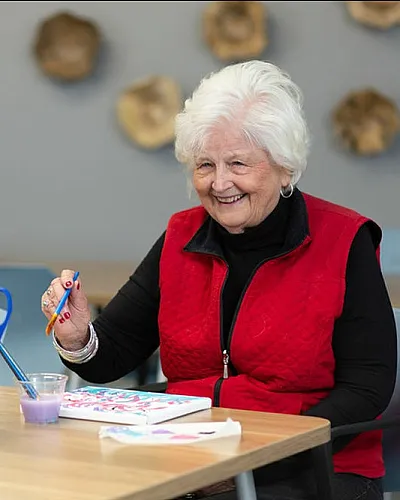 Joyful senior woman painting with vibrant colors at a creative art studio, surrounded by an array of art supplies.