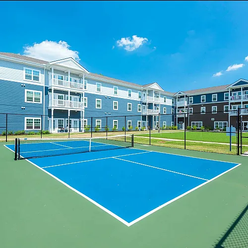 Modern apartment complex with beautiful tennis court under a clear blue sky, perfect for active living and relaxation.