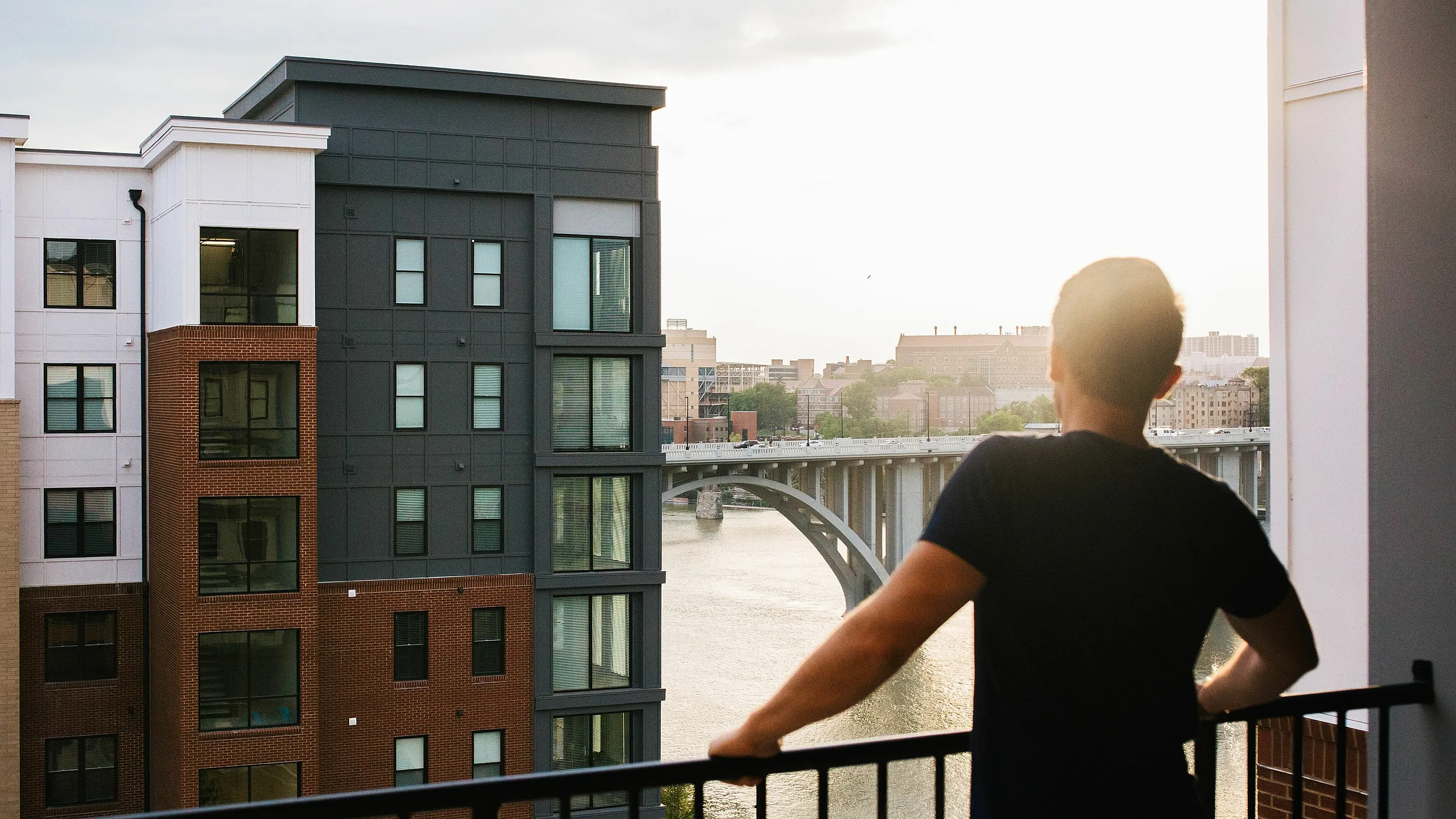 Scenic apartment balcony view overlooking a serene river and city skyline at sunset, featuring modern architectural design.