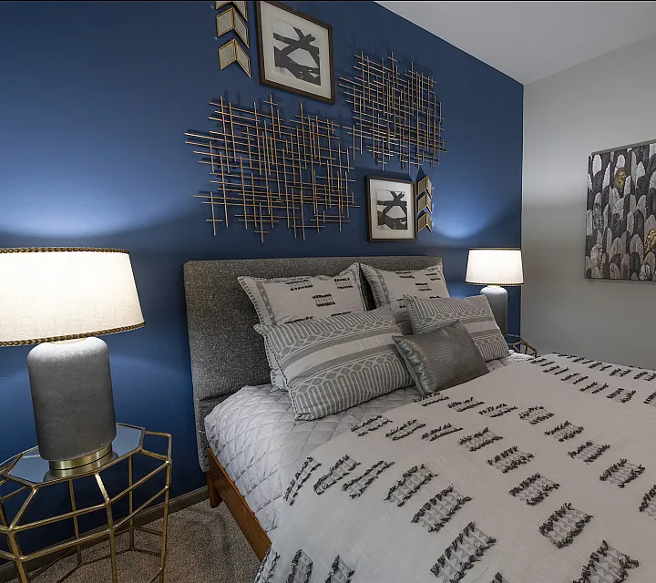 Chic bedroom with a modern design featuring a cozy bed adorned with patterned pillows, a stylish geometric side table with a lamp, and bold wall art against a vibrant blue accent wall.
