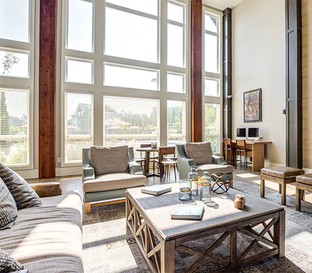 Bright and spacious living room with floor-to-ceiling windows, stylish furniture, and a cozy office nook.