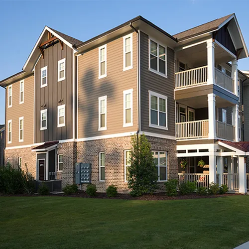Charming three-story apartment building with modern architecture, featuring spacious balconies and surrounded by lush green landscaping.