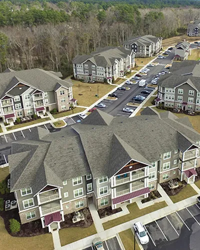Charming aerial view of a modern apartment complex surrounded by lush greenery, showcasing spacious parking and elegant architecture.