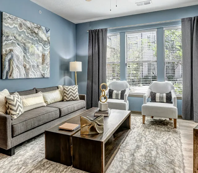 Chic living room with modern decor, featuring a stylish gray sofa, elegant artwork on blue walls, and large windows inviting natural light.