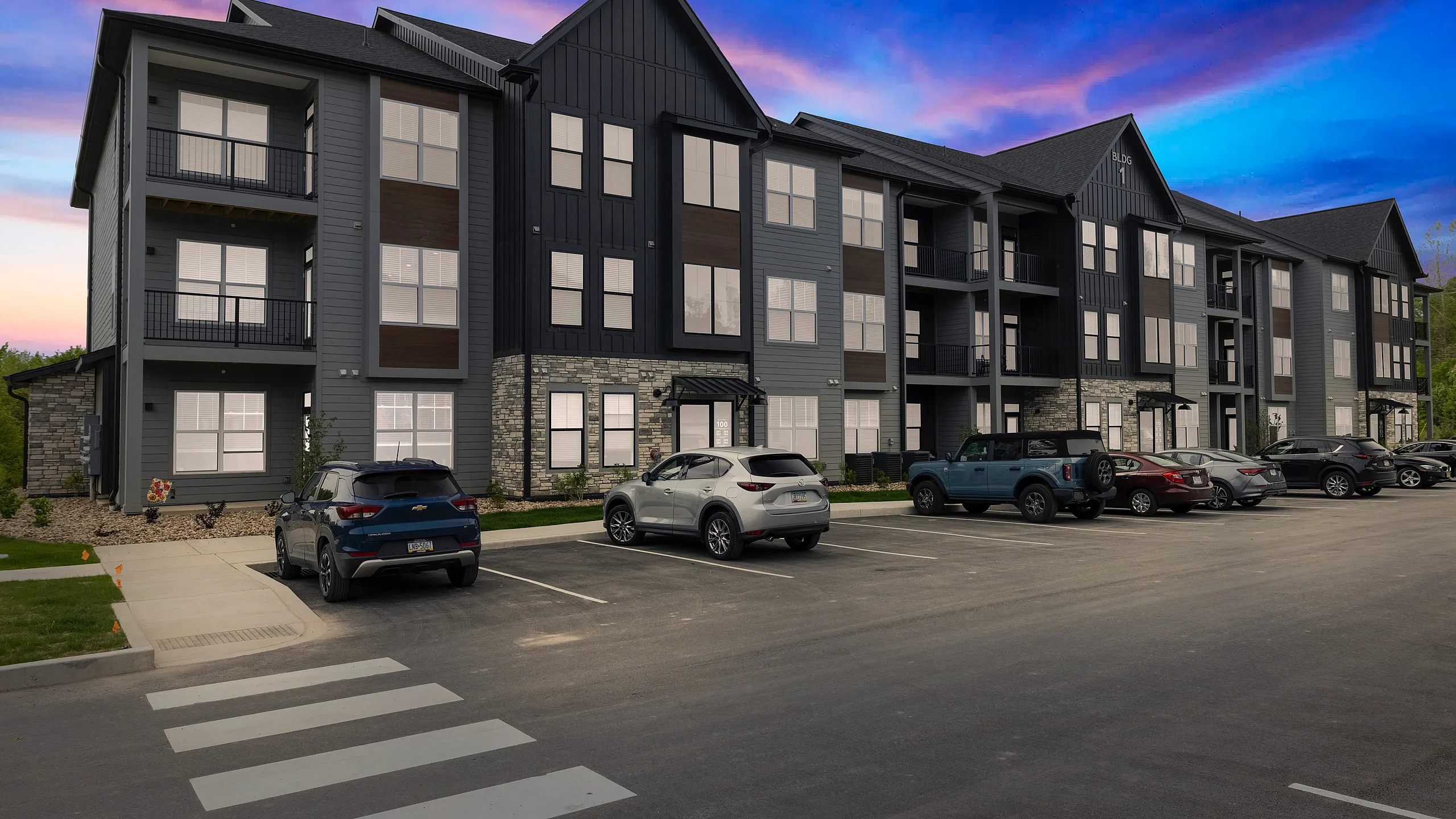 Modern apartment complex with stylish facade and ample parking, set against a vibrant sunset sky.