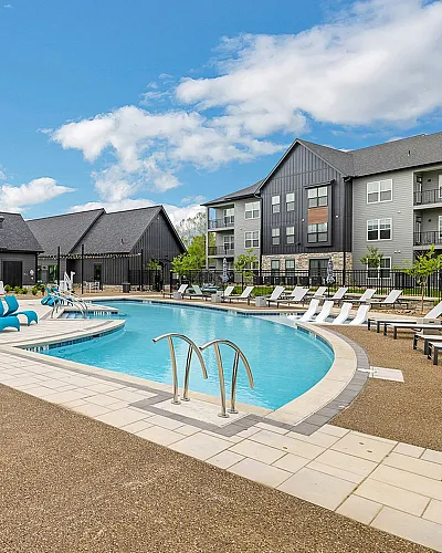 Luxurious apartment complex featuring a sparkling outdoor pool surrounded by modern loungers and stylish buildings under a bright blue sky.