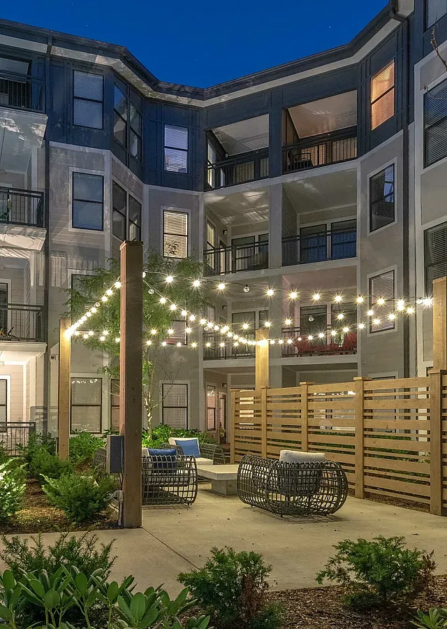 Charming apartment courtyard illuminated by elegant string lights, featuring cozy seating areas surrounded by lush greenery.