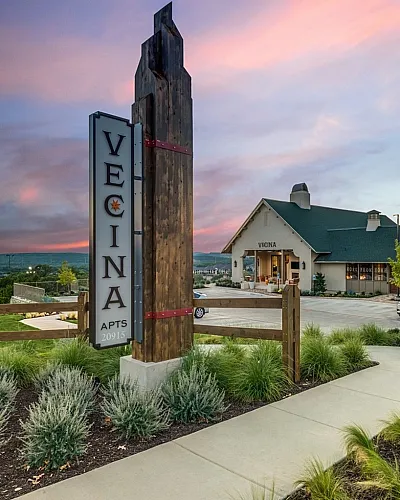 Charming Vecina Apartments entrance featuring lush landscaping and striking architecture at sunset.