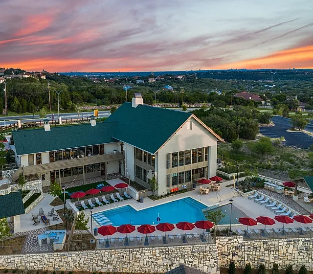 Breathtaking aerial view of modern apartment community with a sparkling pool, sunset skies, and lush greenery.