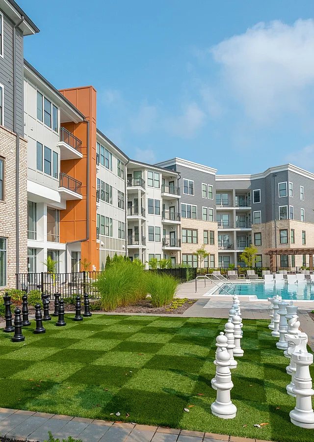 Modern apartment complex with a vibrant courtyard featuring a large chess set and an inviting swimming pool.