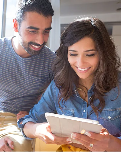 Smiling couple enjoying a bright, sunlit room with large windows and contemporary decor, creating a welcoming atmosphere.