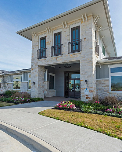 Elegant apartment entrance with beautiful stone facade, large windows, and well-maintained landscaping.