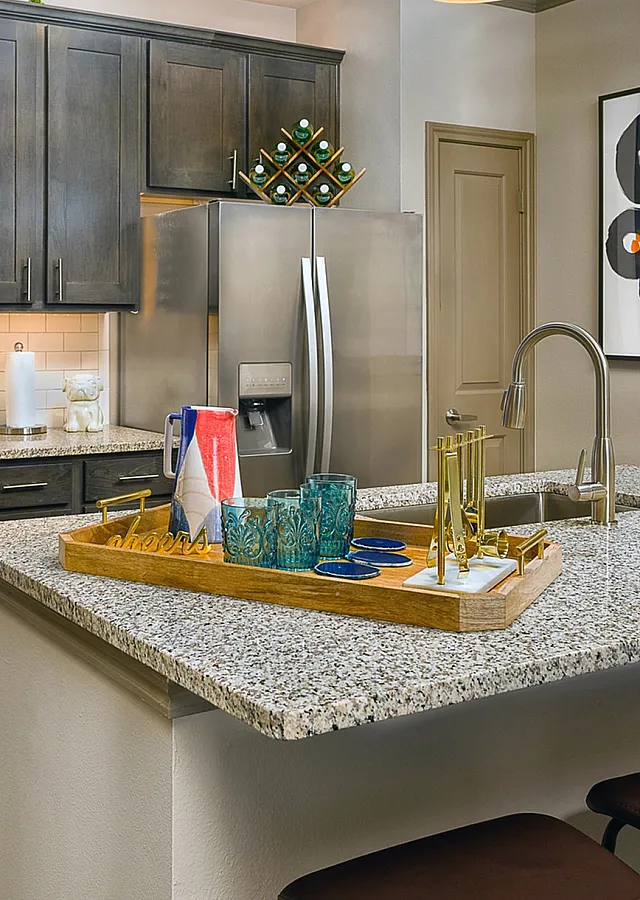 Modern kitchen with granite countertops, stylish wooden cabinetry, and a decorative tray on the island, featuring elegant glasses and chic decor.