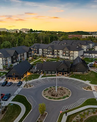 Captivating aerial view of a modern apartment complex at sunset, surrounded by lush greenery and ample parking space, offering a serene suburban lifestyle.