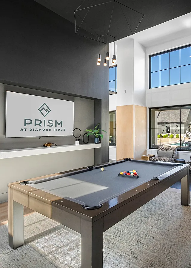 Modern recreation room at Prism featuring a sleek pool table, contemporary decor, and large windows for natural light.