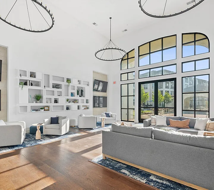 Modern and spacious living area with high ceilings, large windows, and elegant decor. Cozy seating arrangements and stylish shelving enhance the chic ambiance.