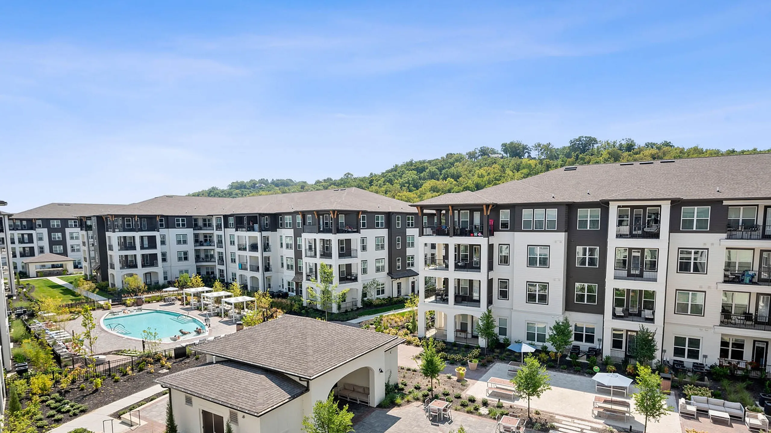Elegant apartment complex featuring modern architecture, beautifully landscaped grounds, and a luxurious swimming pool under a clear blue sky.