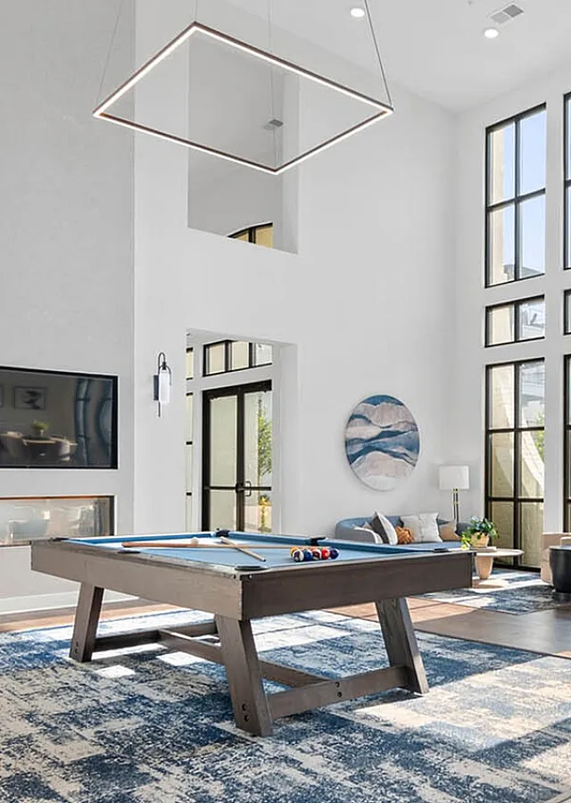 Luxurious lounge area featuring high ceilings, large windows, and a modern billiards table, accentuated by chic decor and natural light.