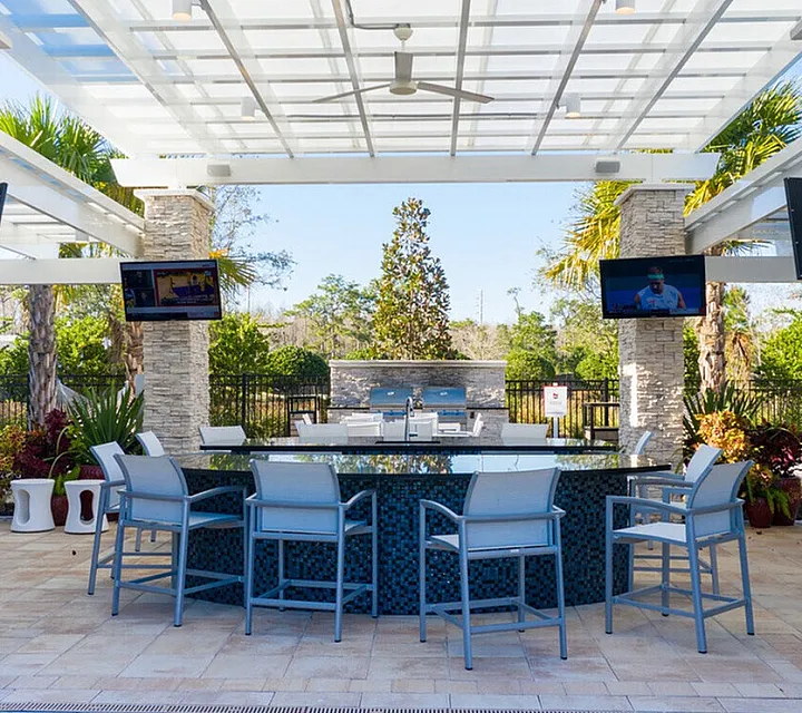 Luxurious outdoor lounge area with modern bar seating, stone pillars, and vibrant greenery under a chic pergola.
