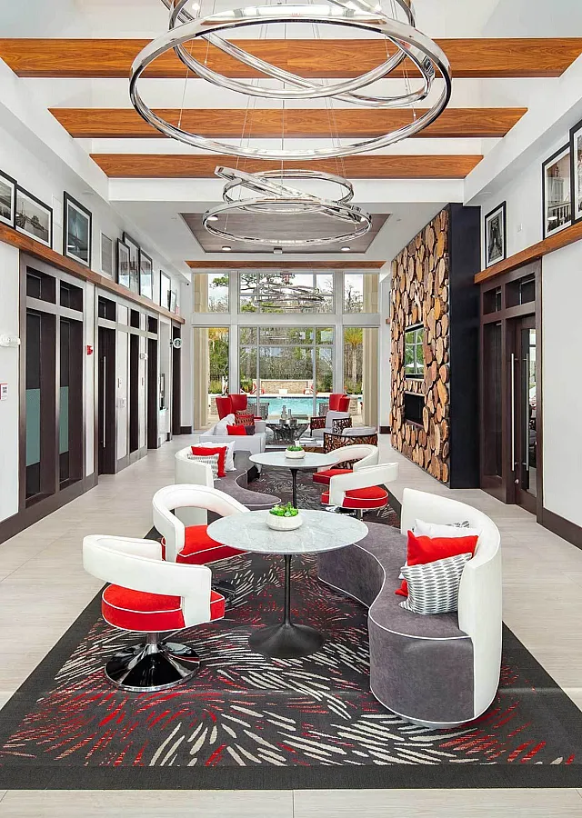 Chic lobby area with modern decor, featuring stylish circular chandeliers, vibrant red and white chairs, and a cozy fireplace with a contemporary log design.