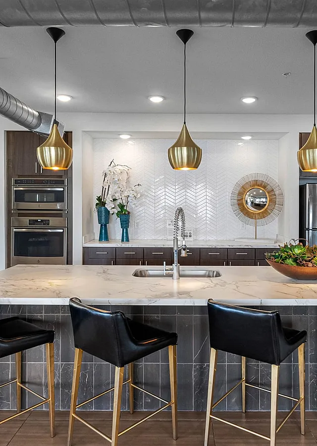 Modern kitchen with elegant marble island, sleek appliances, and chic pendant lighting, featuring a sophisticated open office space in the background.