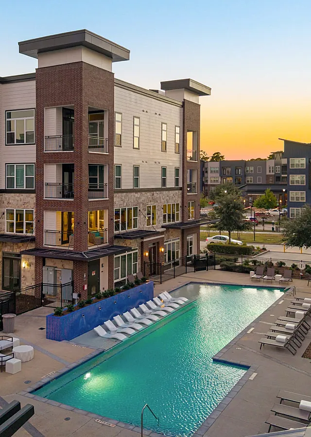 Modern apartment complex with a sparkling swimming pool, surrounded by stylish multi-story buildings at sunset.