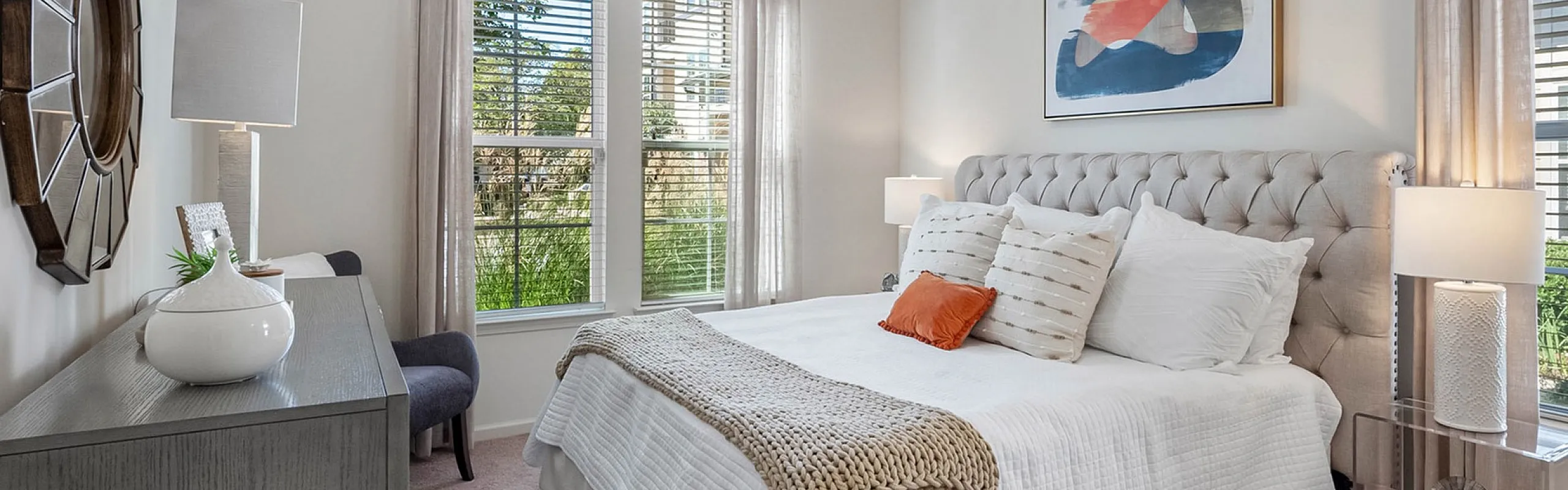 Inviting bedroom featuring a plush bed with decorative pillows, modern artwork, and large windows allowing natural light to flood the room.