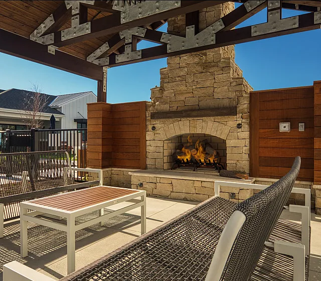 Inviting outdoor patio featuring a cozy stone fireplace, stylish seating, and a backdrop of modern architecture.