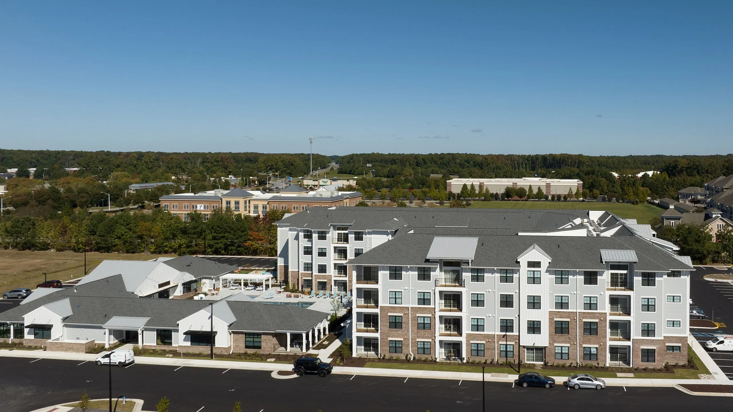 Aerial view of a modern apartment complex surrounded by lush greenery and ample parking, showcasing a peaceful residential area with easy access to local amenities.