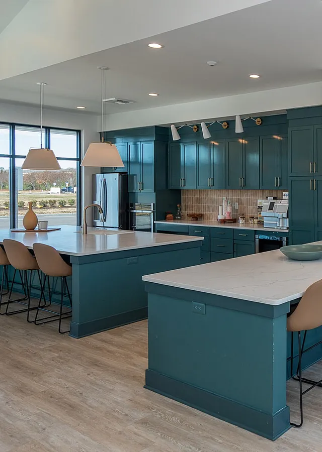 Bright contemporary kitchen with teal cabinets, spacious island seating, and elegant pendant lighting, offering scenic views through large windows.