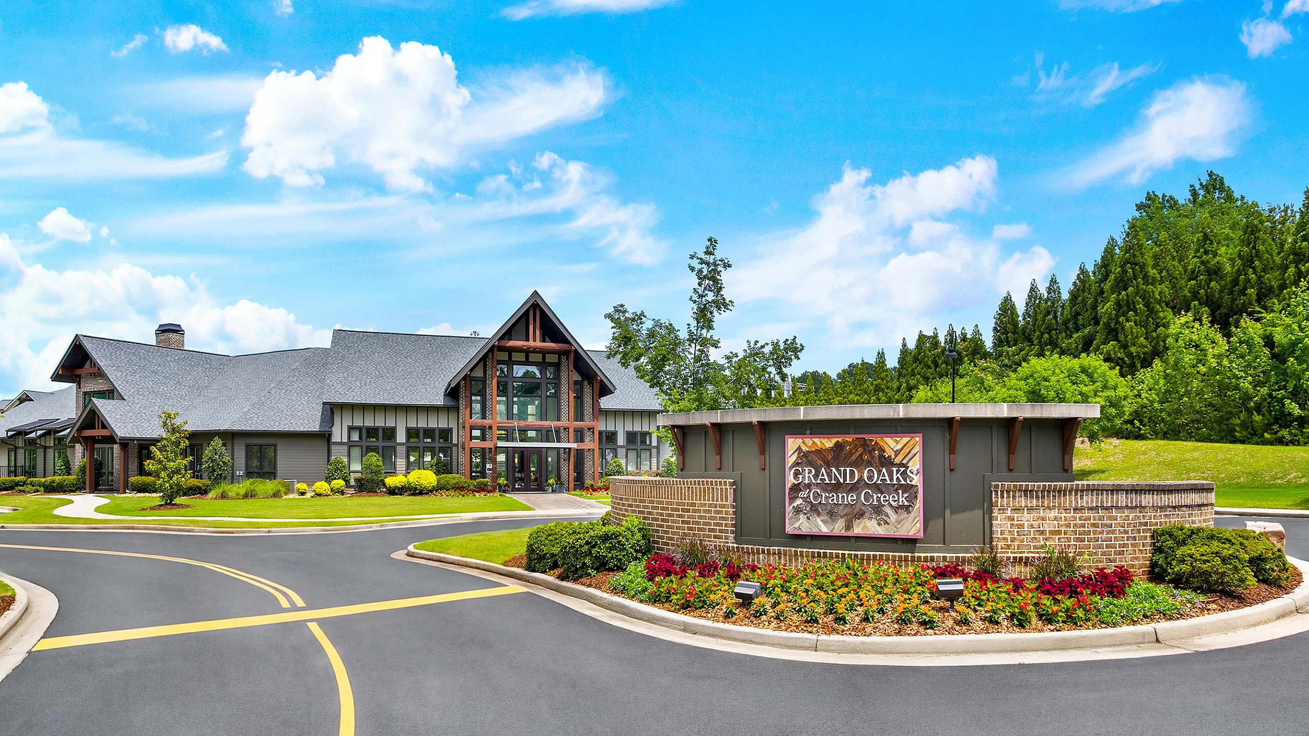 Inviting entrance to Grand Oaks at Crane Creek, featuring modern architecture and vibrant landscaping against a bright, clear sky.