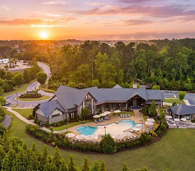 Breathtaking aerial view of a luxurious property surrounded by lush greenery, featuring a stunning pool and elegant architecture at sunrise.