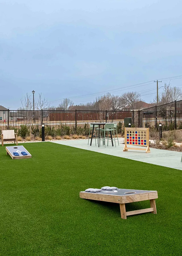 Inviting outdoor recreation area with lush green lawn, cornhole games, and seating under an open sky.